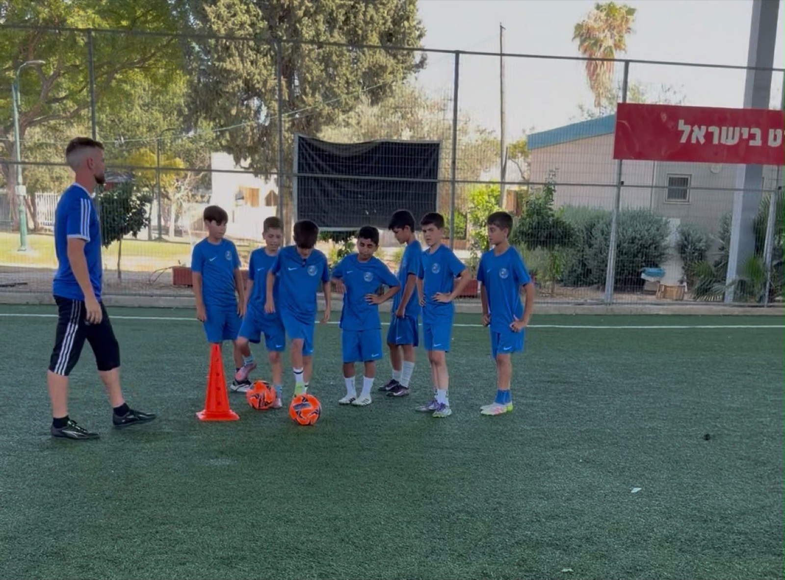 קבוצת ילדים עומדים ליד קונוסים וכדורים במגרש, לפני תרגיל